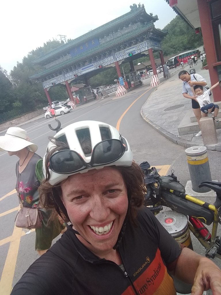 Coffee First Book Tour Edinburgh. Jenny Graham's Pedal Powered Book Tour. Image shows  Jenny standing in front of her bike with a Chinese road toll-gate in the background