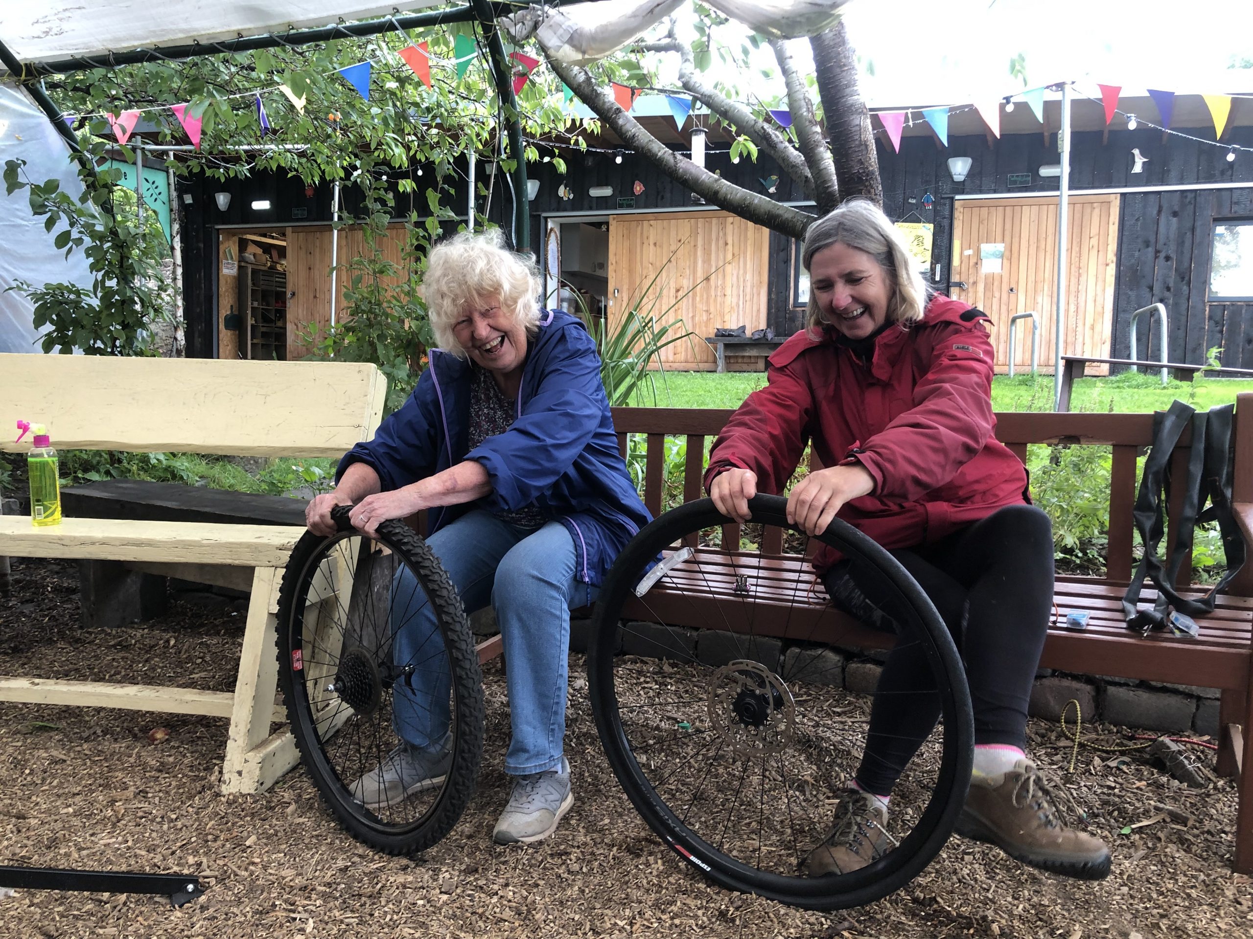 Bridgend Farmhouse Basic bike maintenance class. Image shows two women who are part of a bike maintenance class putting tyres back onto their bicycle wheels