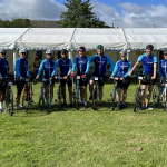 The photo show the Cycle Law Scotland legal team dresses in their cycle team kit, with their bikes at an event. There is a large marquee in the background