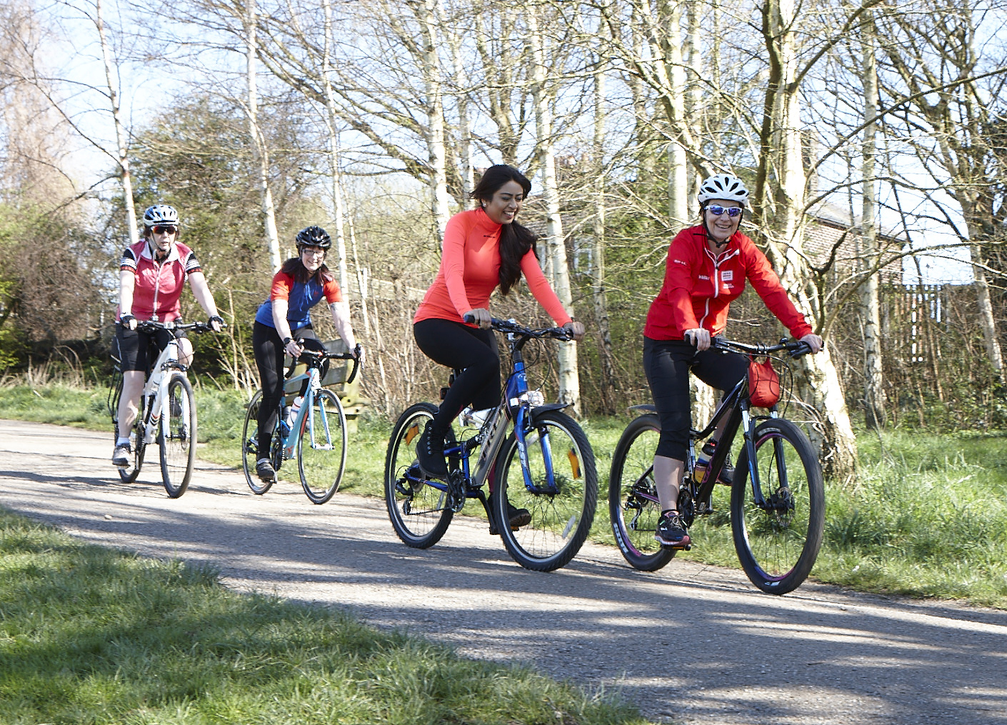 Photo shows four women cycling along a quiet off road path with trees in the background