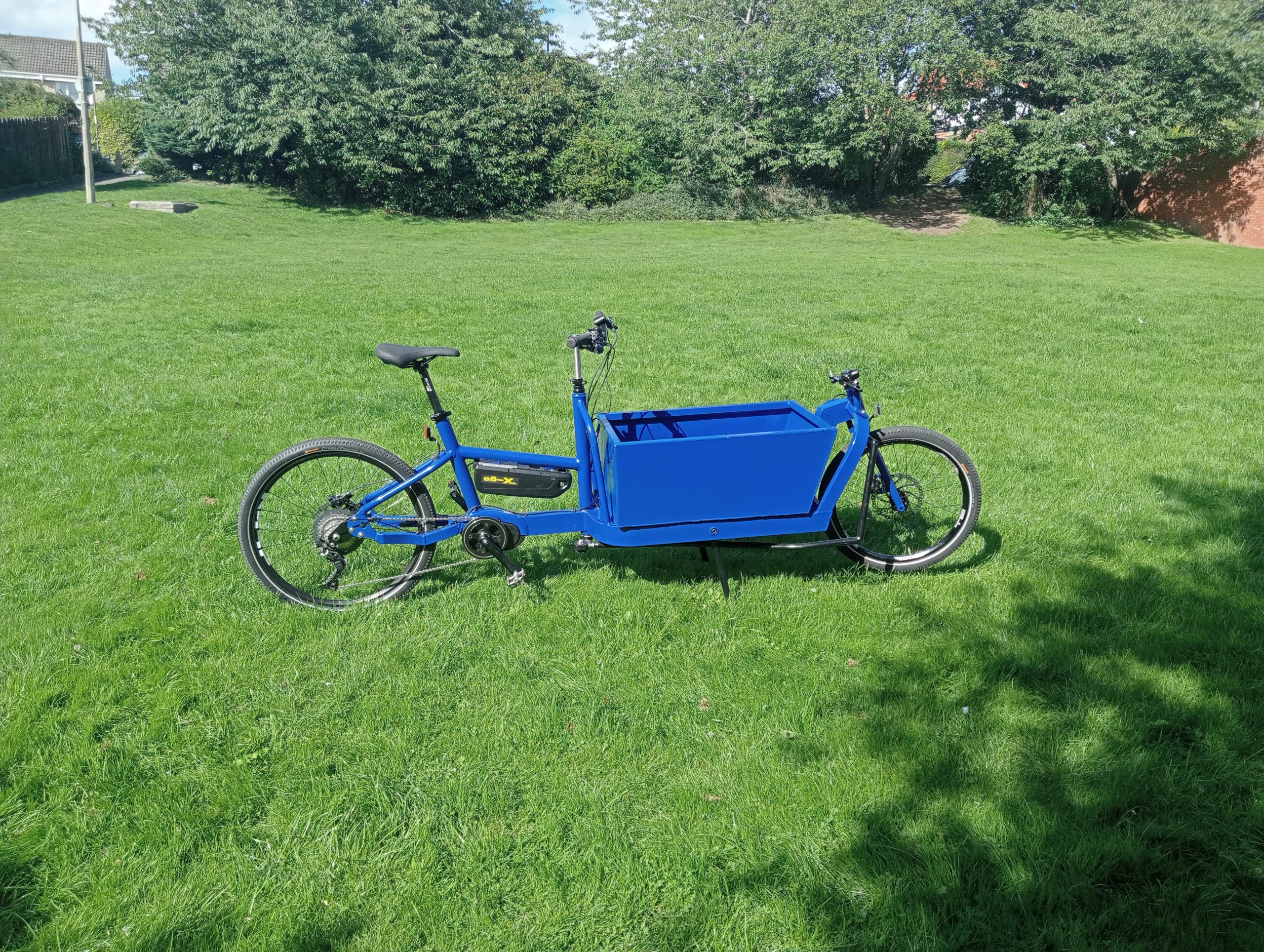 Photo shows a blue cargo bike in a field of grass