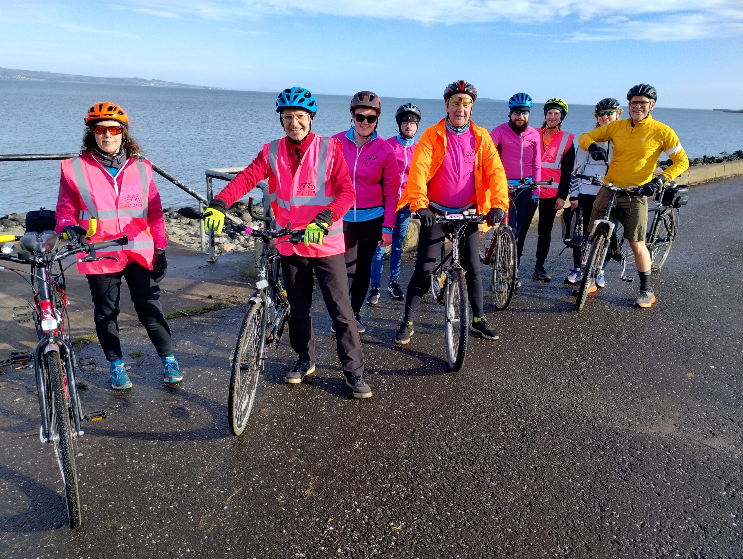 Image shows a group of people tandem bicycles, on a path next to the sea.